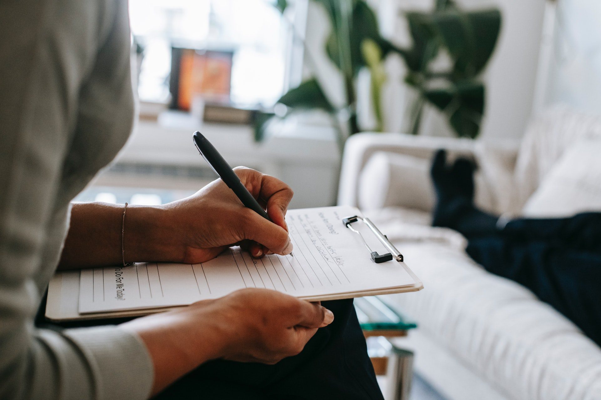 Crop ethnic psychologist writing on clipboard during session<br />
